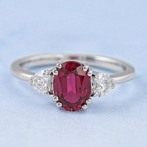 front view of oval red ruby gemstone & heart diamond three stone engagement ring