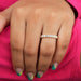 Round Cut Lab Grown Diamond Eternity Wedding Band displayed on a woman's hand with colorful nail art, set against a vibrant pink background.