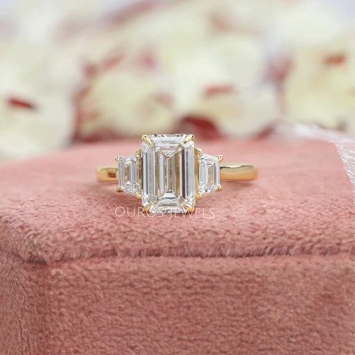3 stone emerald cut diamond ring kept on soft ring box 
