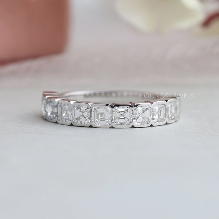 Asscher Cut Diamond Half Eternity Wedding Band is displayed on white soft surface with a blurred floral background