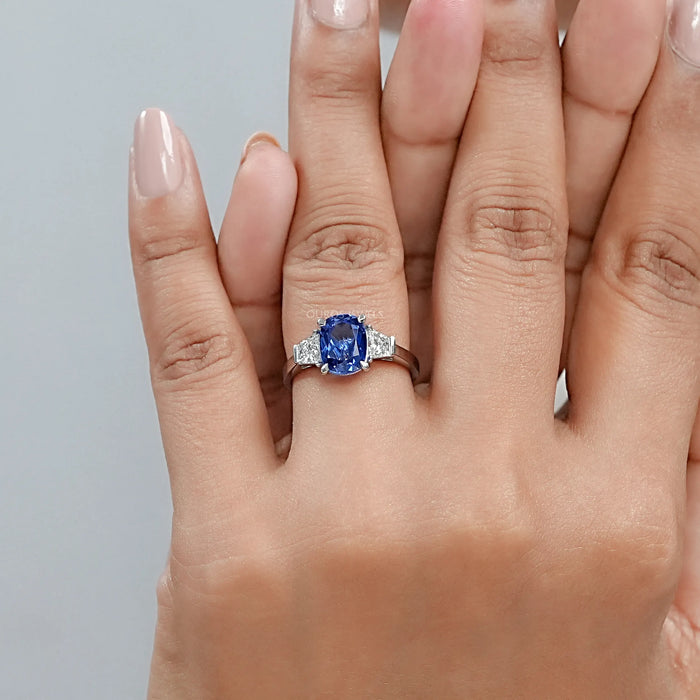 sapphire cushion gemstone with trapezoid diamond 3 stone wedding ring on model's finger
