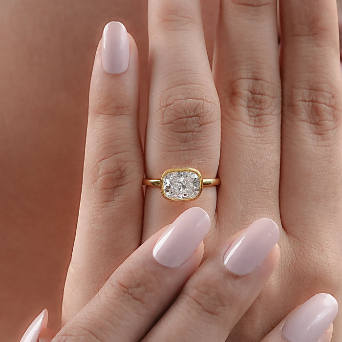 east west cushion cut diamond bezel set engagement ring in finger