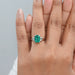 green emerald gemstone with trapezoid diamond 3 stone engagement ring in finger