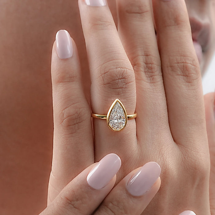 pear cut diamond bezel set solitaire engagement ring in finger