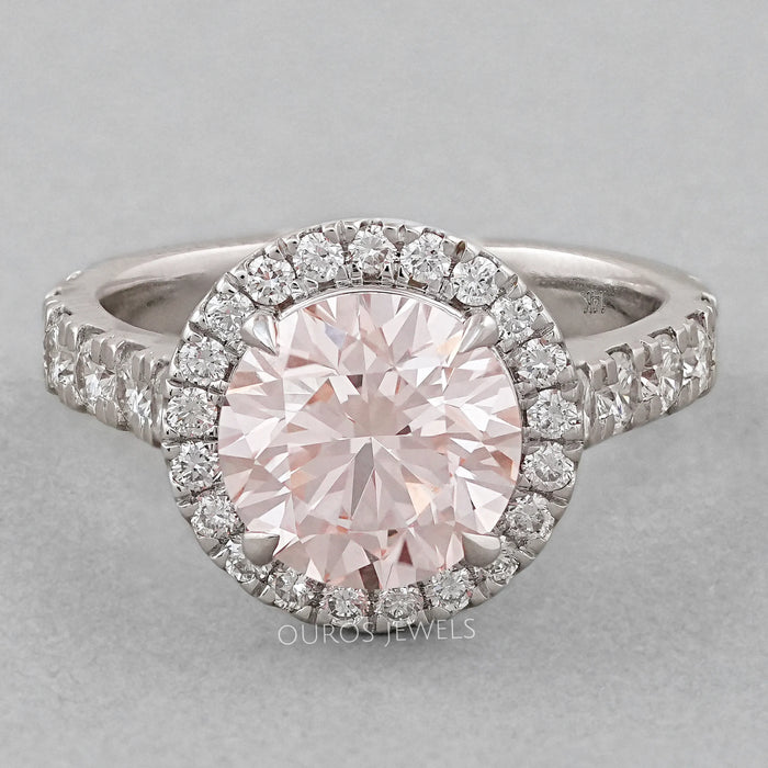 front view of pink round-cut diamond solitaire halo engagement ring on grey fabric