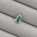 1.62 Carat Fancy Vivid Green Pear Cut Lab Grown Diamond on a light grey fabric background, highlighting its vivid green color and pear shape.