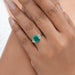 green emerald gemstone with trapezoid diamond 3 stone engagement ring on model's finger