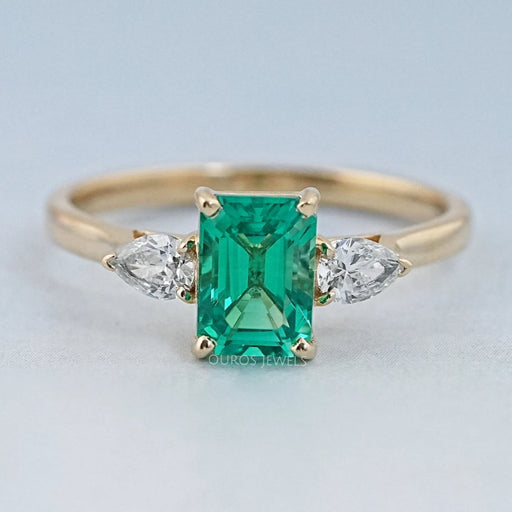 front view of green emerald gemstone and pear diamond three stone engagement ring