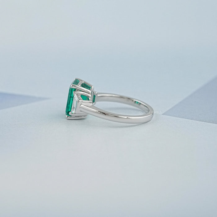 side view of green emerald gemstone with trapezoid diamond 3 stone engagement ring
