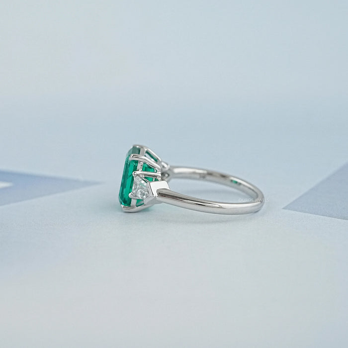 left view of emerald gemstone and bullet-cut diamond three-stone engagement ring