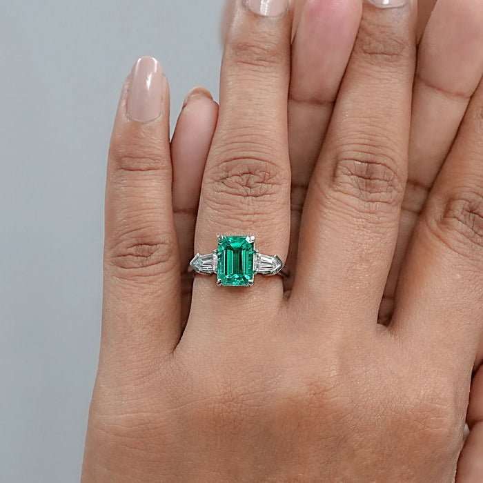 emerald gemstone and bullet-cut diamond three-stone engagement ring in finger