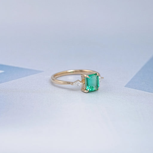 side view of green emerald gemstone and kite cut three stone engagement ring