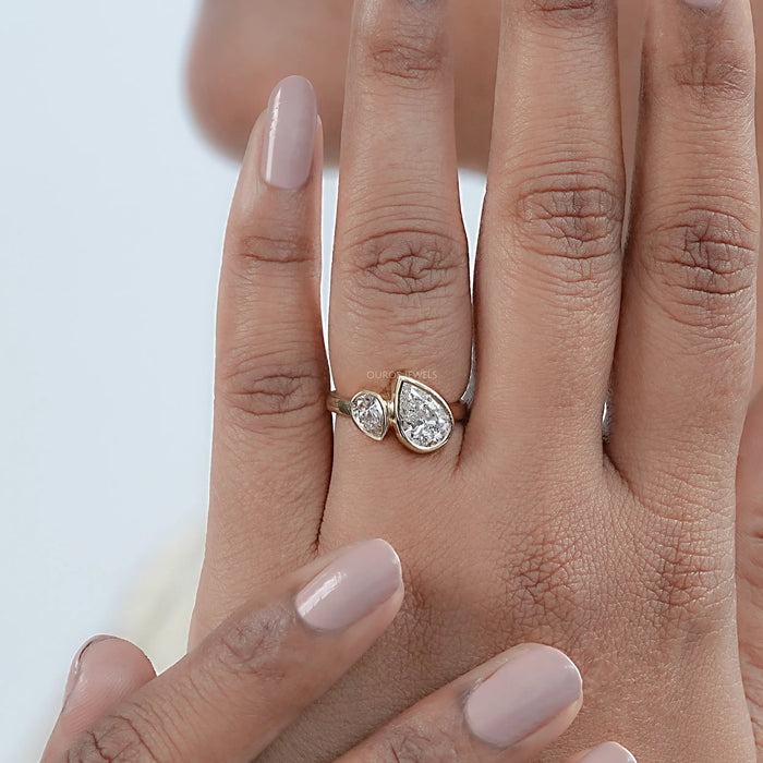 top view of two stone pear shaped diamond bezel set engagement ring in finger