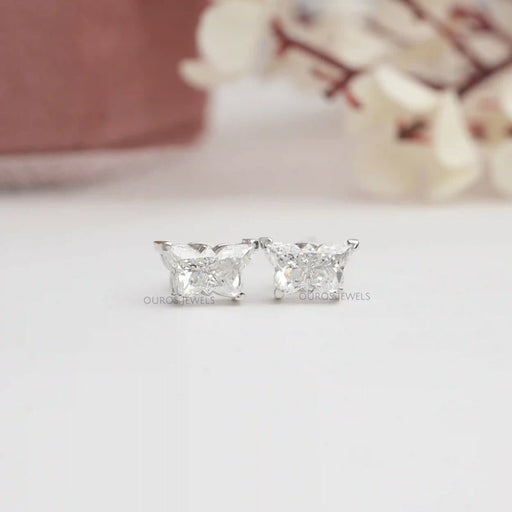 Butterfly Cut Diamond Stud Earrings featuring two sparkling diamonds set against a soft, blurred floral background.