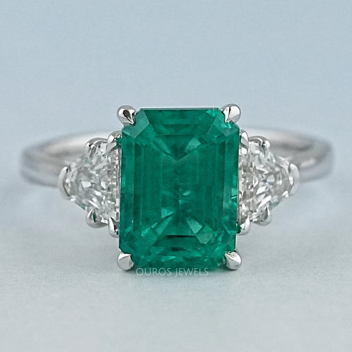 front view of green emerald gemstone with shield cut diamond 3 stone engagement ring