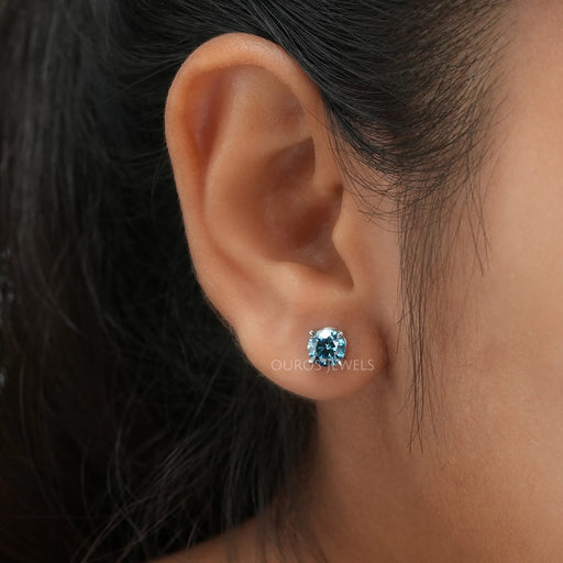  Blue Round Diamond Stud Earrings worn on an ear, showing the brilliant blue diamond against the skin.