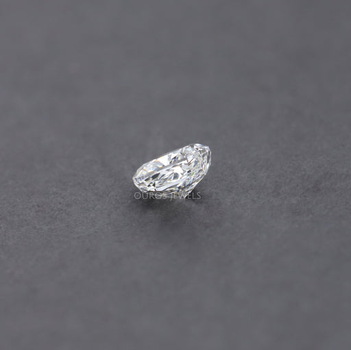 0.70 Carat Brilliant Cushion Cut Lab Diamond resting on a dark, textured surface, showcasing its sparkling clarity and detailed from a side angle.
