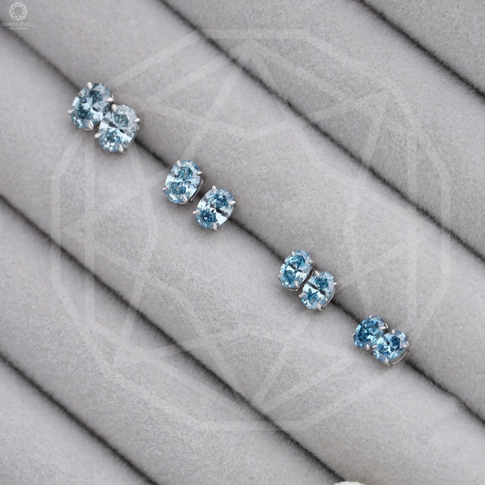 Blue Oval Cut Lab Diamond Stud Earrings displayed on a gray fabric holder, showcasing their sparkle and elegance in a tiered arrangement.